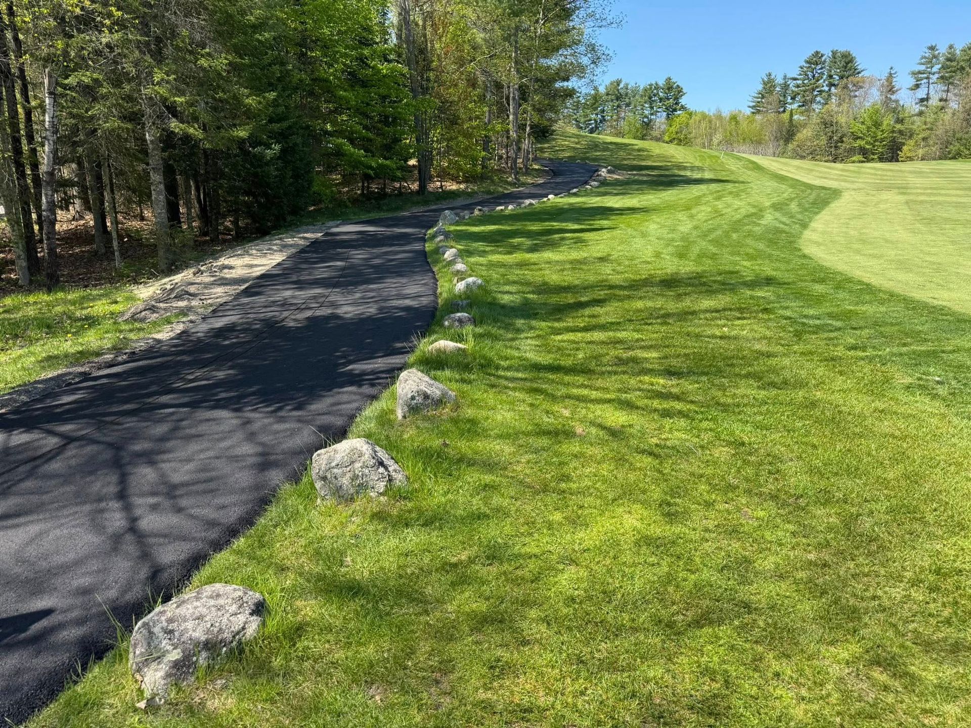 A dirt road going through a grassy field next to a golf course.