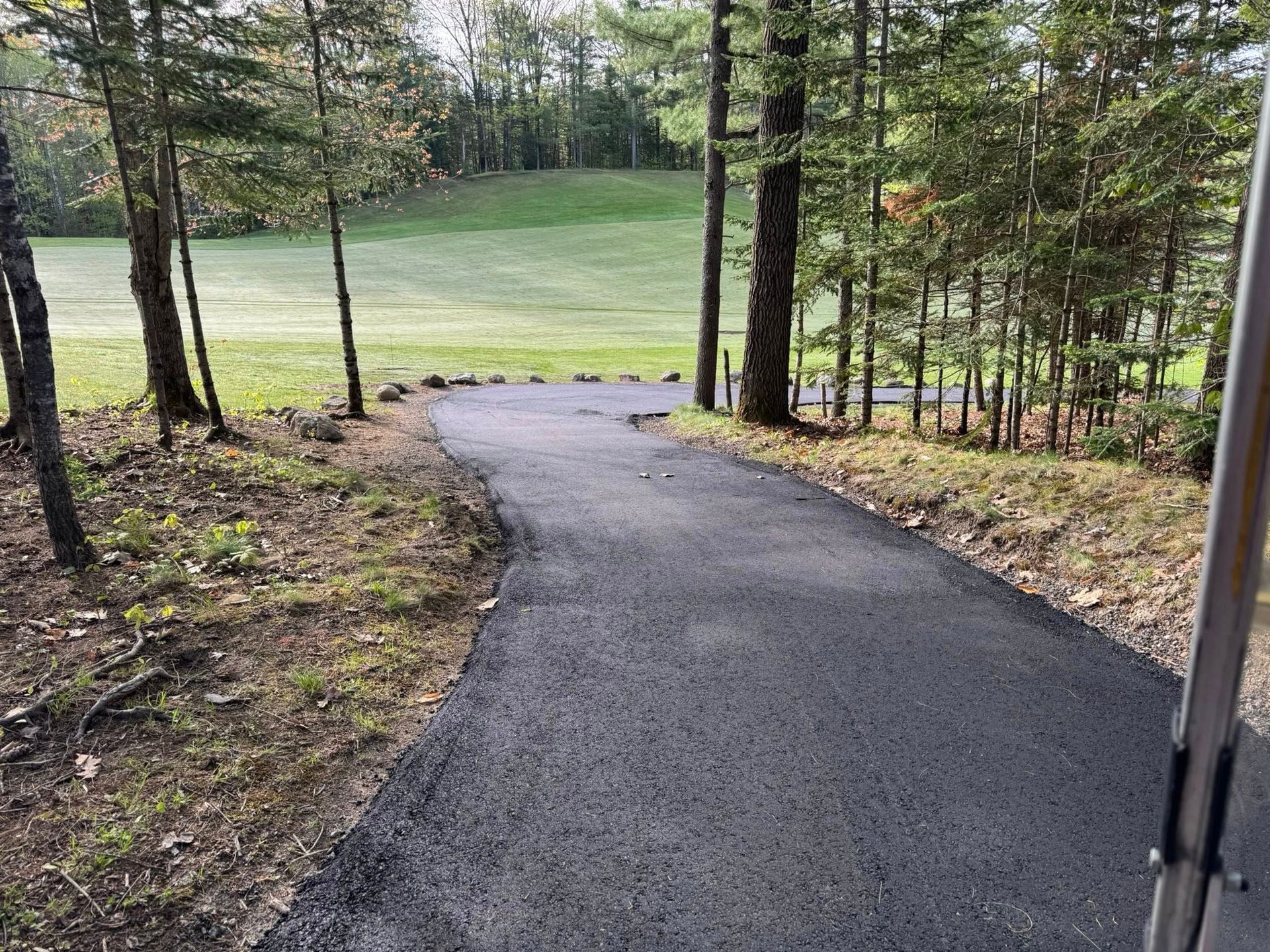 A path leading to a golf course surrounded by trees.