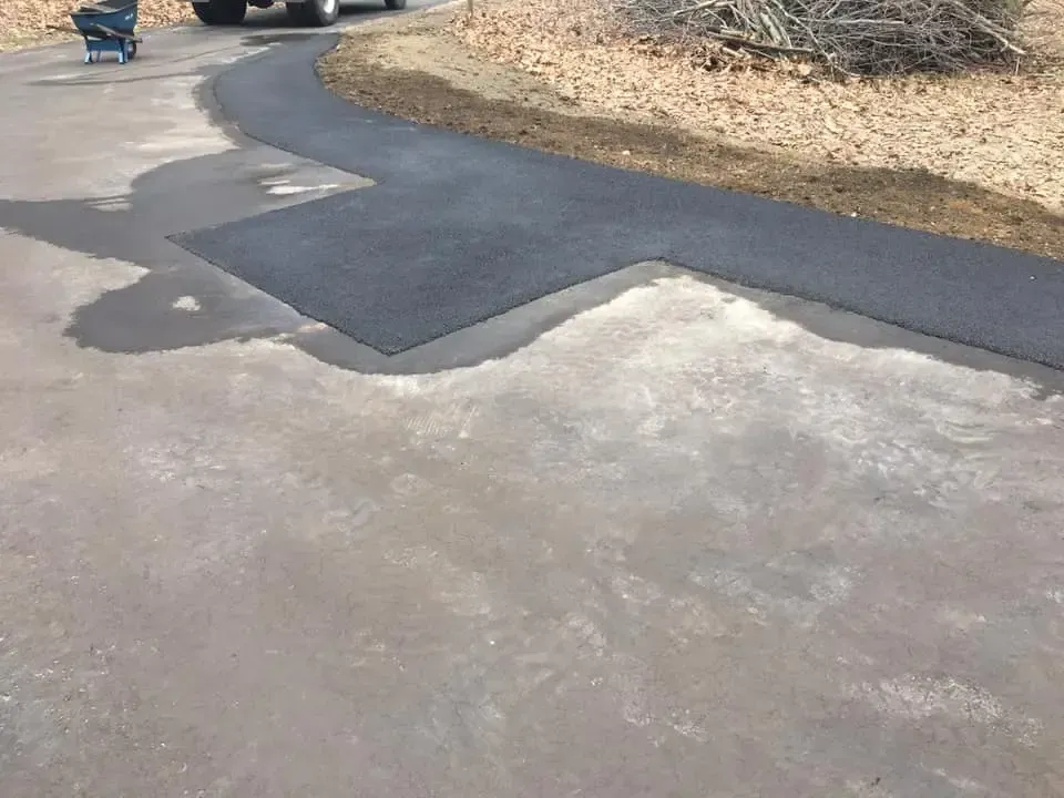 A car is parked in a driveway next to a wheelbarrow.