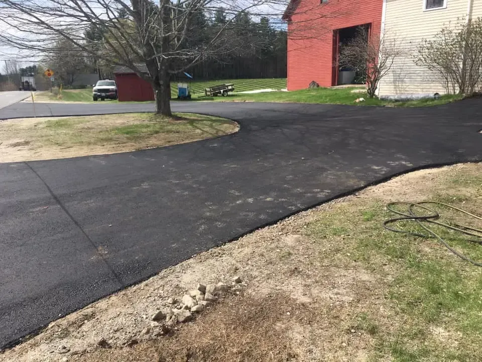 A driveway leading to a house with a red barn in the background.