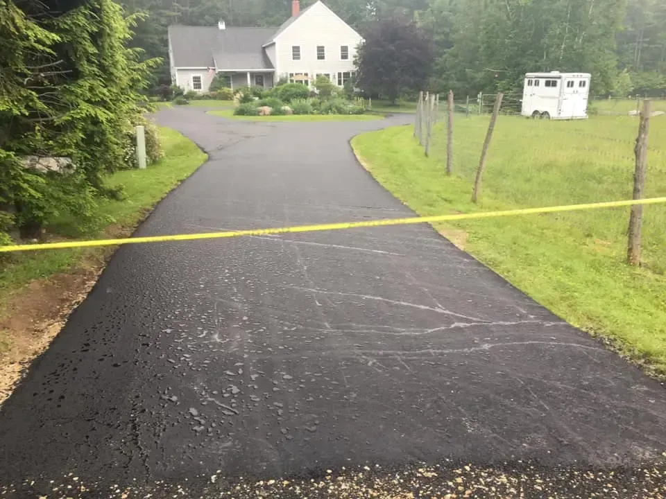 A road with a yellow tape along the side of it and a house in the background.