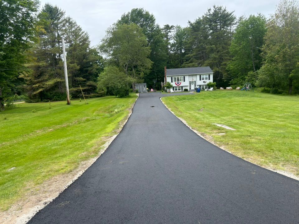 A driveway leading to a house in the middle of a lush green field.