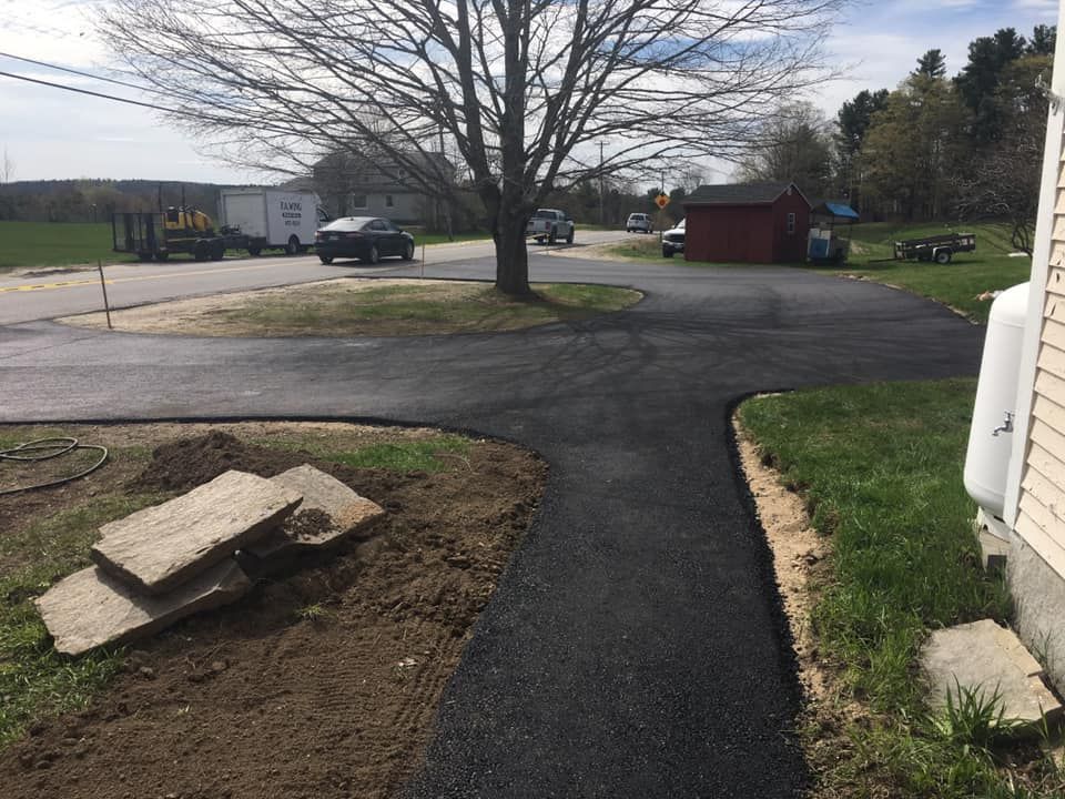 A newly paved driveway leading to a house with a truck parked on the side of the road.