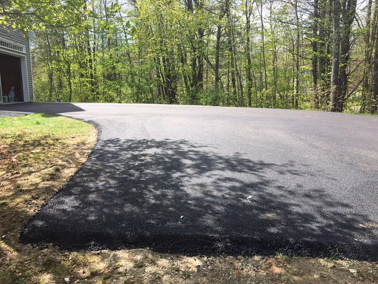 A newly paved driveway leading to a garage in the woods.