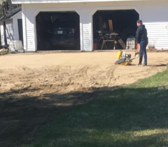 A man is standing in the dirt in front of a garage.