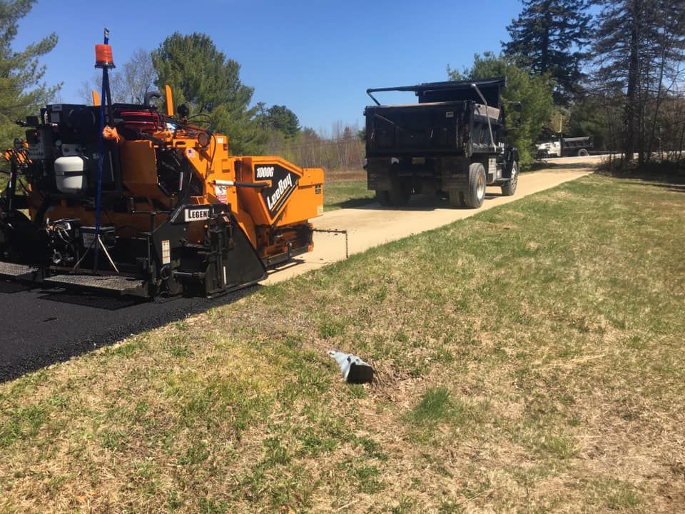 A truck is driving down a road next to a paving machine.