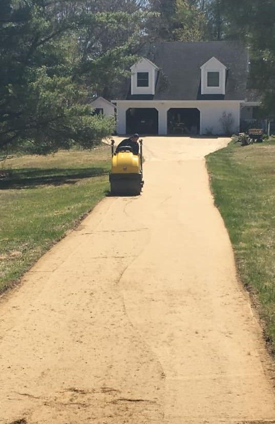 A yellow truck is driving down a dirt road in front of a house.