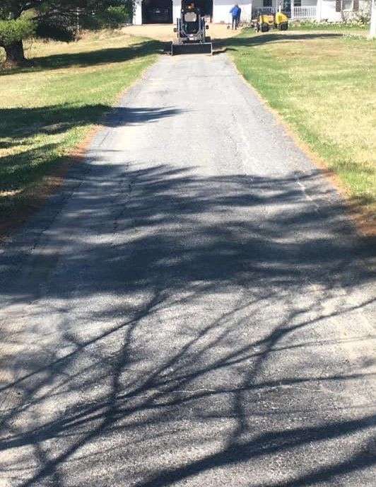 A shadow of a tree is cast on the asphalt of a driveway