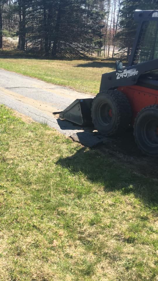 A red and black skid steer is parked in the grass next to a road.