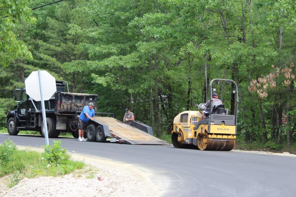 A dump truck is being towed by a roller on the side of the road.