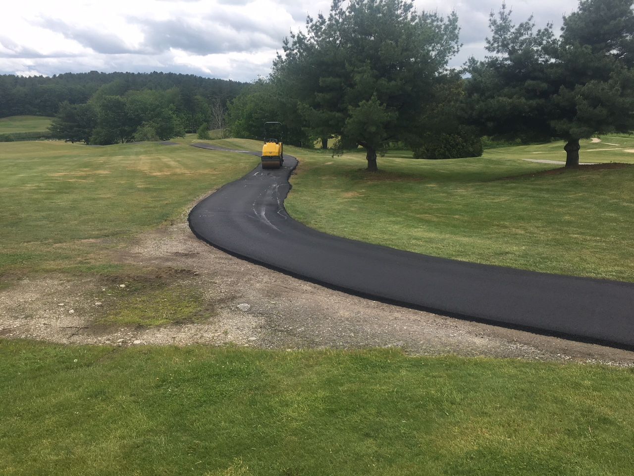 A yellow golf cart is driving down a curvy road.