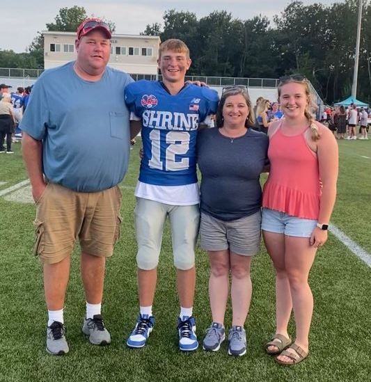 A group of people posing for a picture with one wearing a jersey that says shrine 12