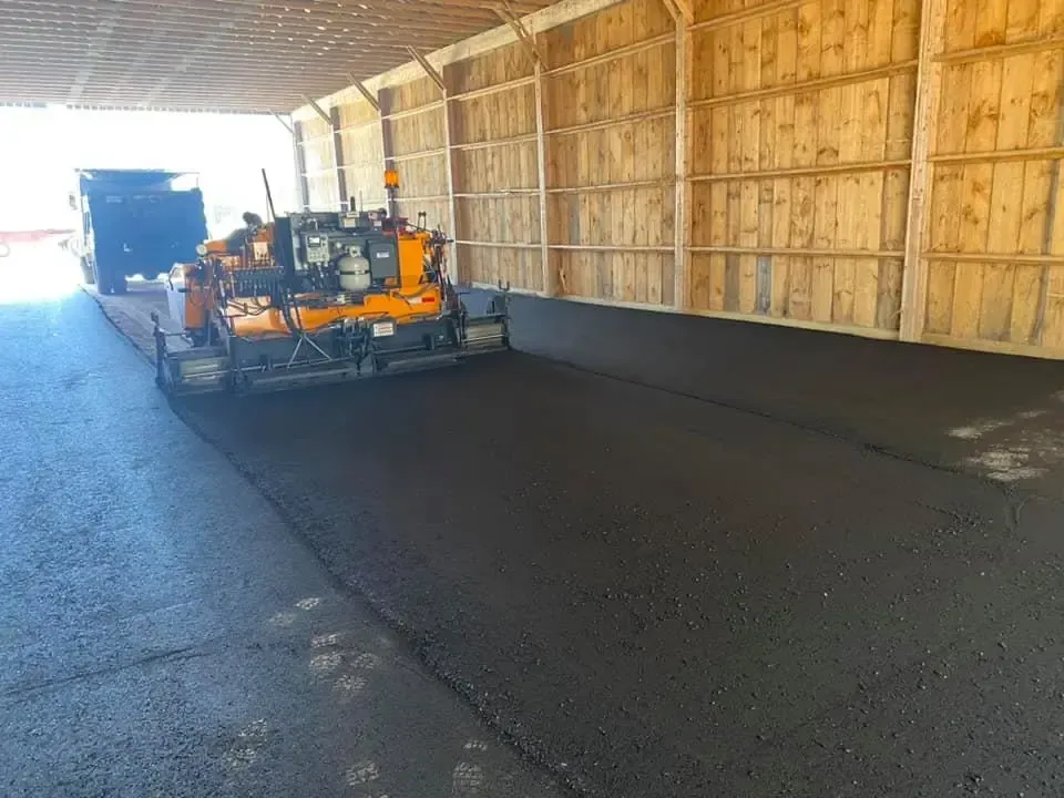 A machine is laying asphalt in a parking lot under a bridge.