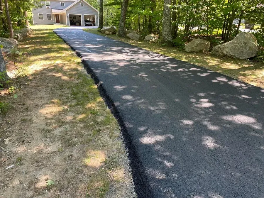 A newly paved driveway leading to a house in the woods.