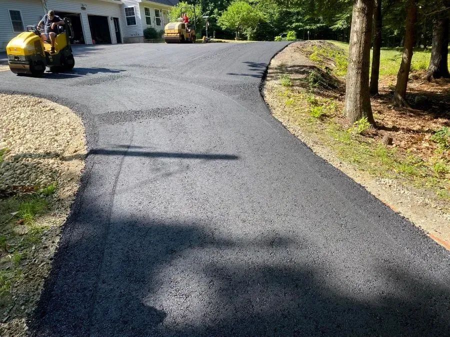 A man is driving a yellow tractor down a newly paved driveway.