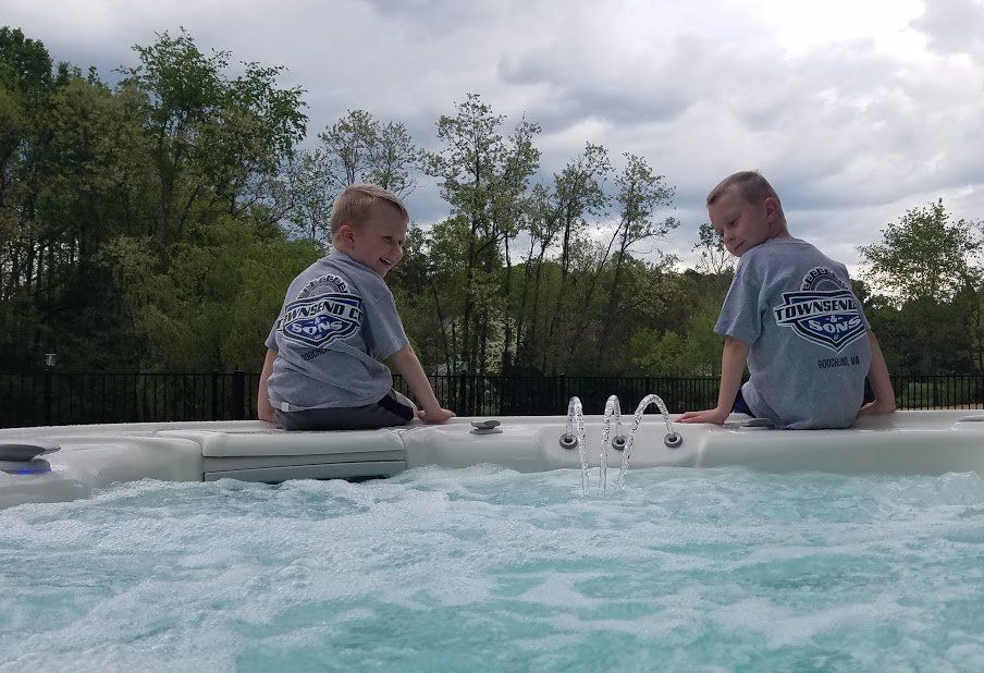 Two young boys are sitting on the edge of a hot tub