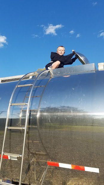 A boy is sitting on top of a large metal tank with a ladder.