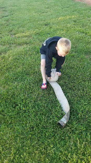 A young boy is playing with a fire hose in the grass.