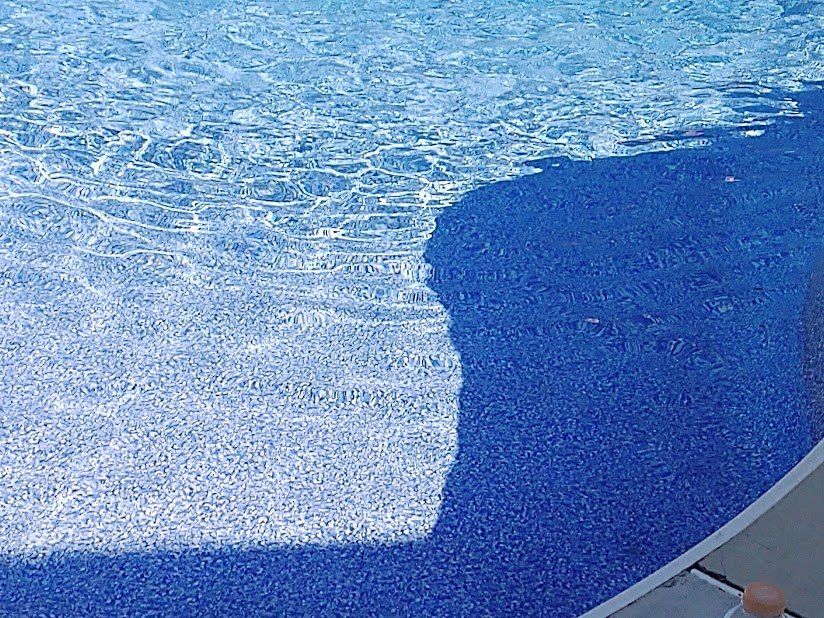 A person 's shadow is cast on the side of a swimming pool.