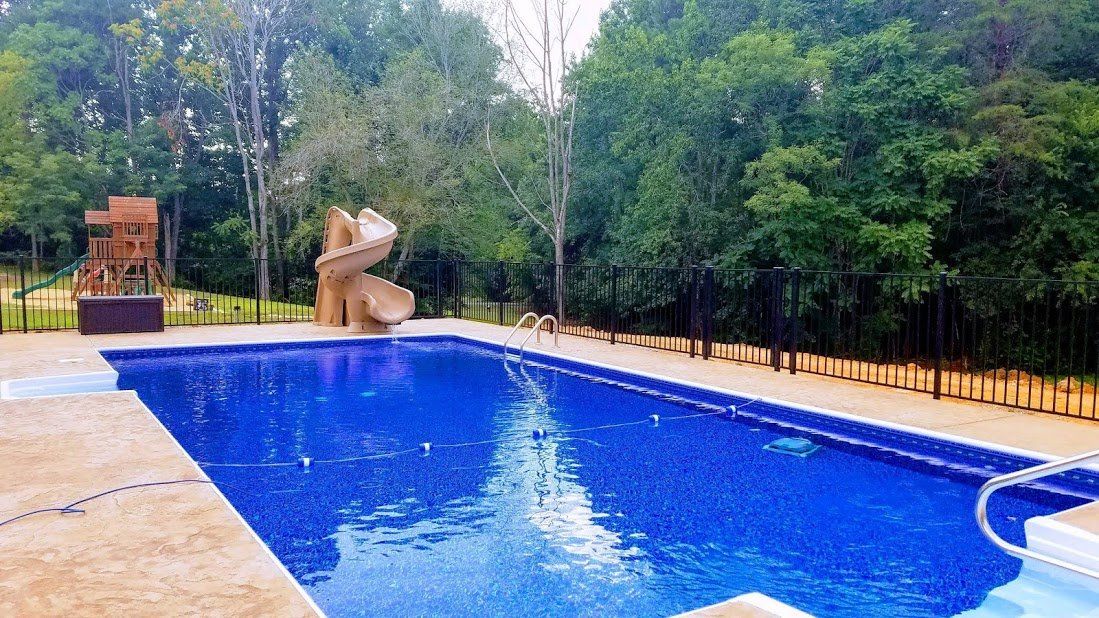 A large swimming pool with a slide in the backyard surrounded by trees.