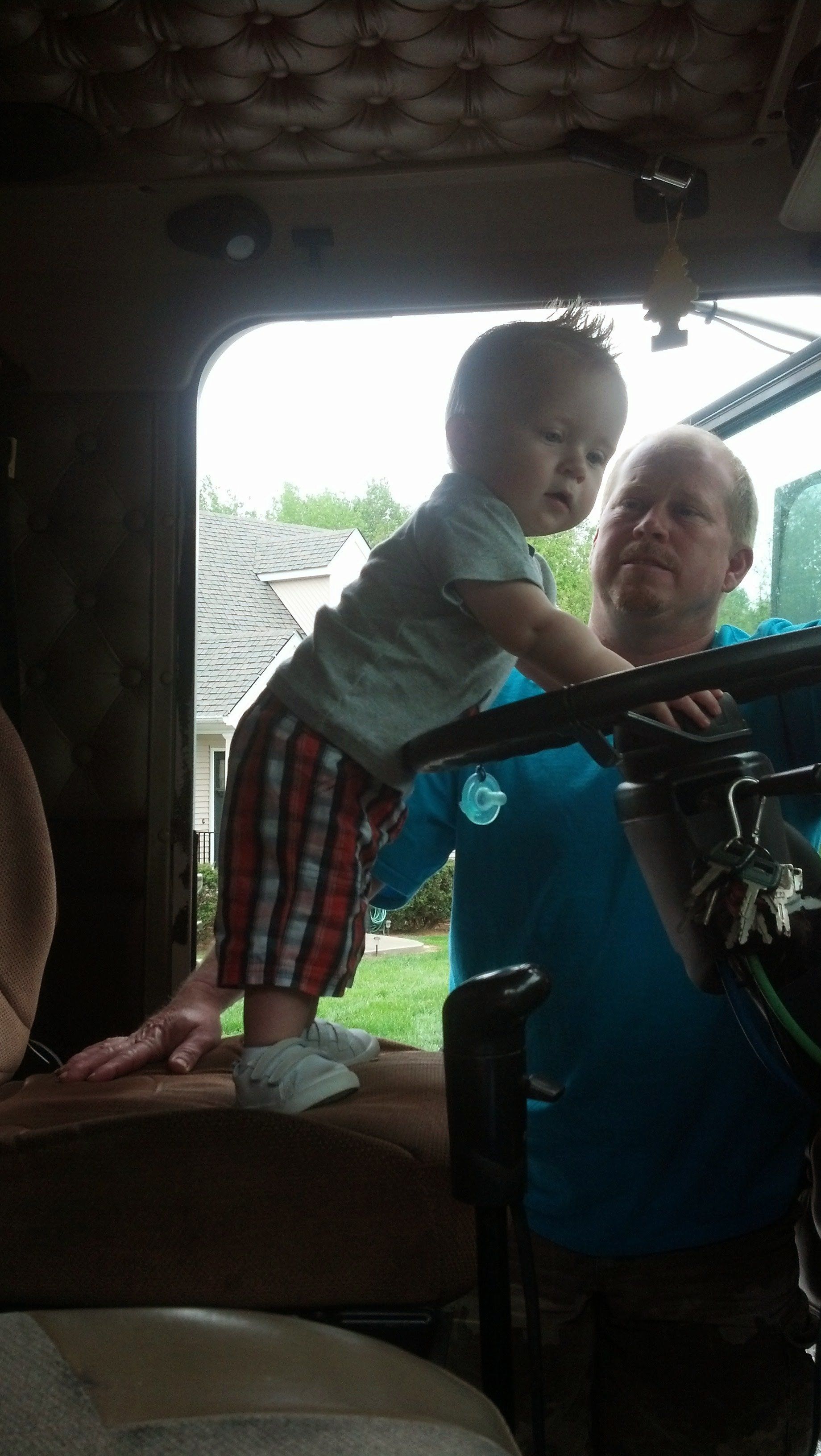 A baby is standing on the steering wheel of a truck.
