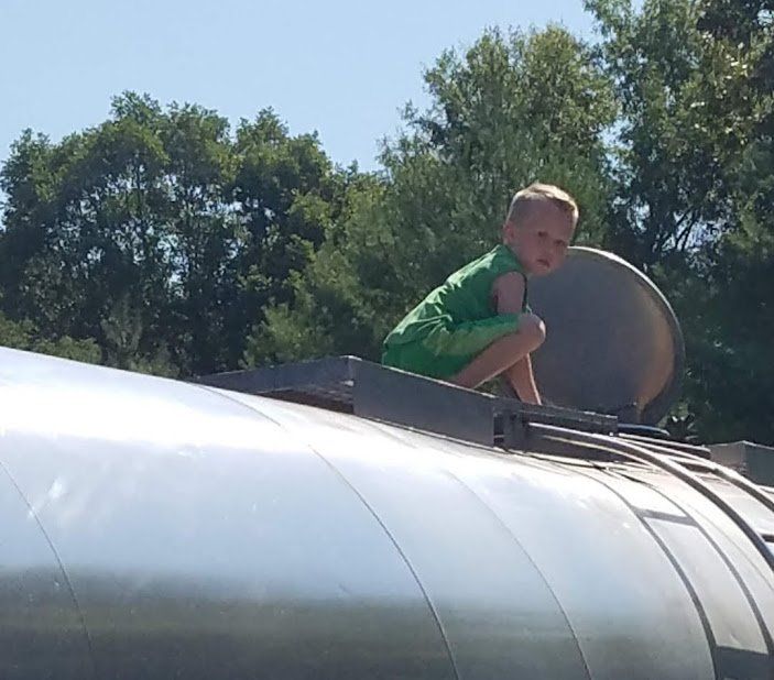 A young boy in a green shirt sits on top of a metal pipe