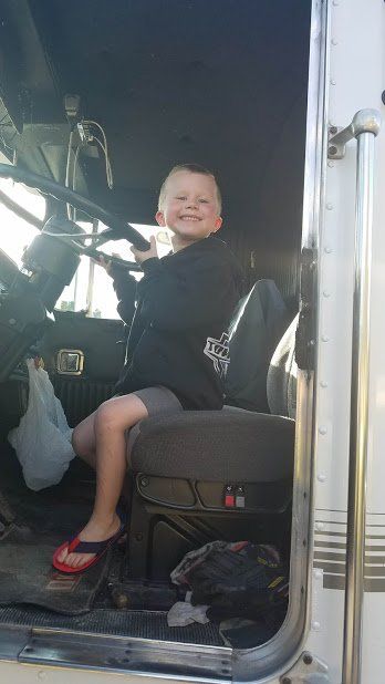 A young boy is sitting in the driver 's seat of a semi truck.