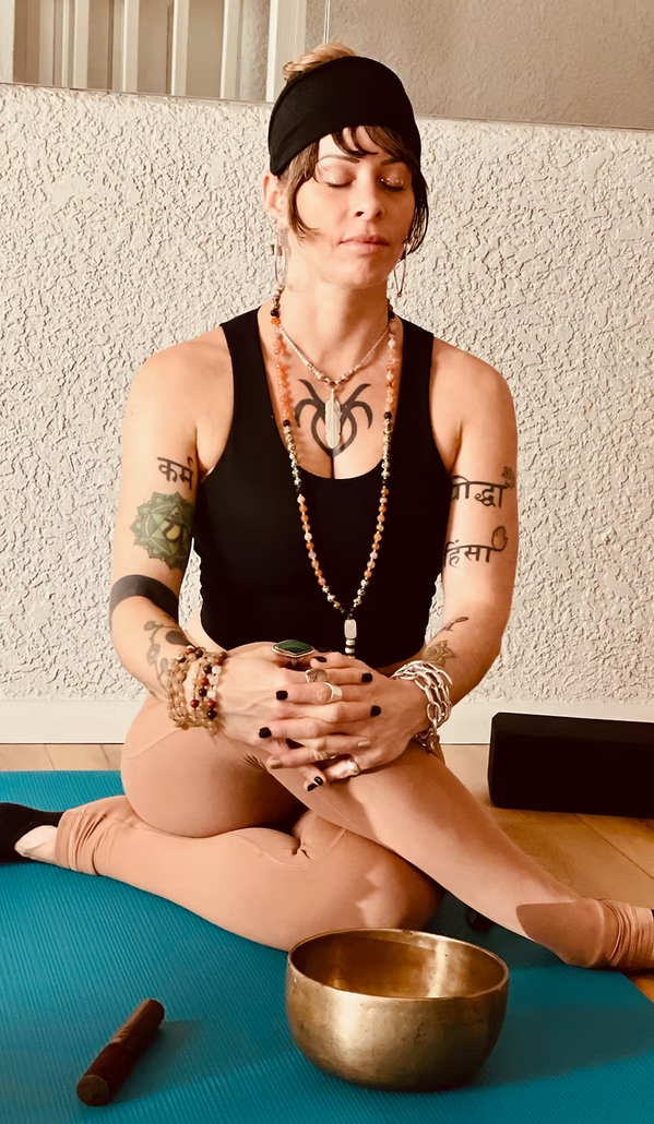 Woman seated cross-legged on a yoga mat, meditating with eyes closed beside a singing bowl.