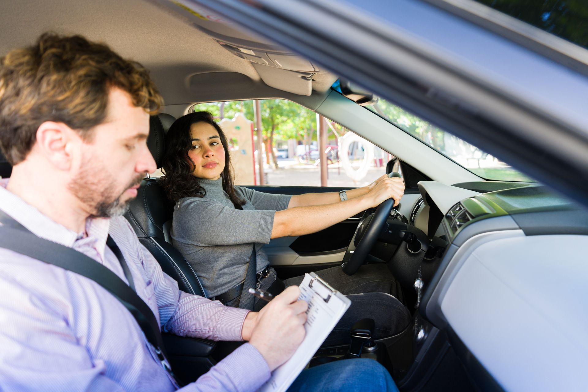 Latin instructor representing teen driving classes as he rates a teen girl driving safely.
