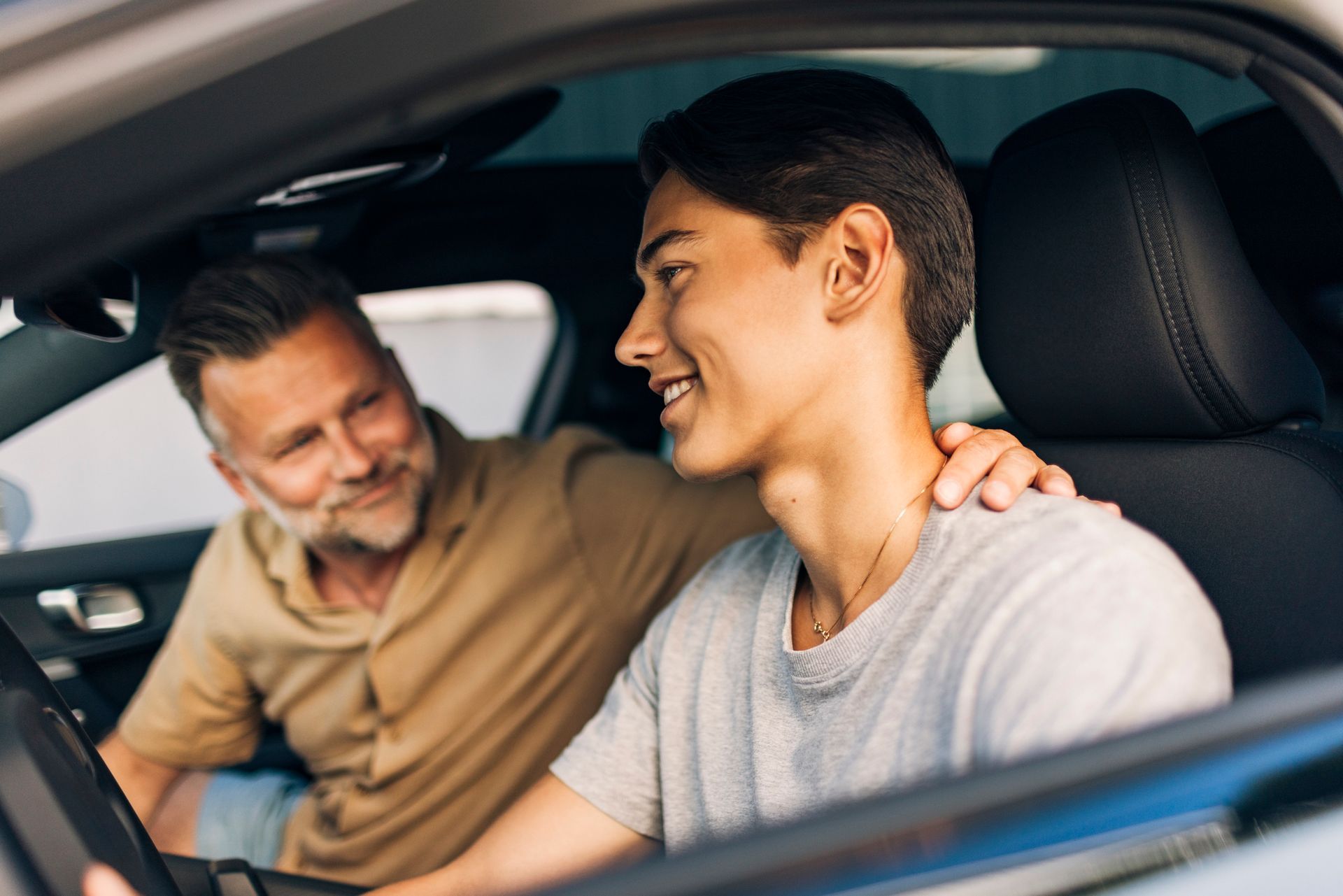 Smiling young man getting driving lessons from father while sitting in car Smiling young man getting driving lessons from father while sitting in car