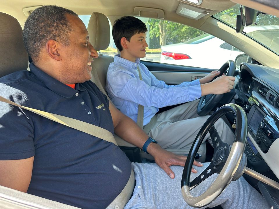 Latin instructor representing teen driving classes as he rates a teen girl driving safely.