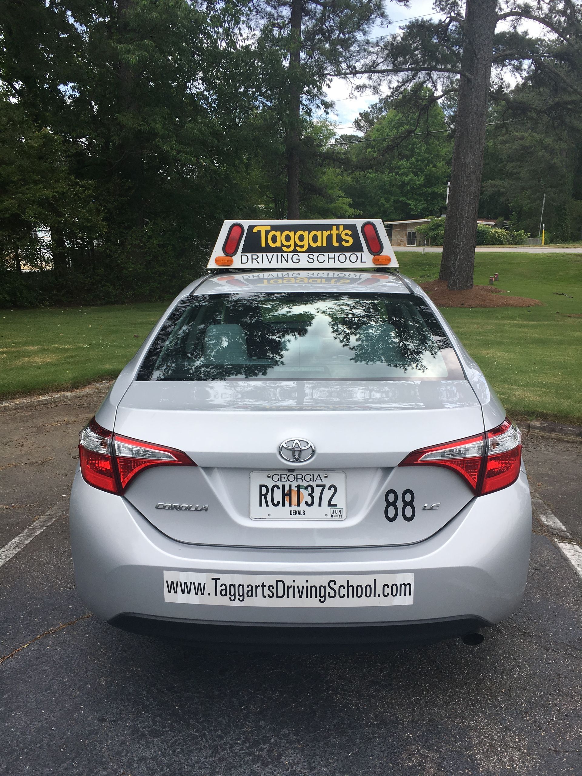 A silver car is parked in a parking lot with trees in the background.  — Tucker, GA — Taggart's Driving School
