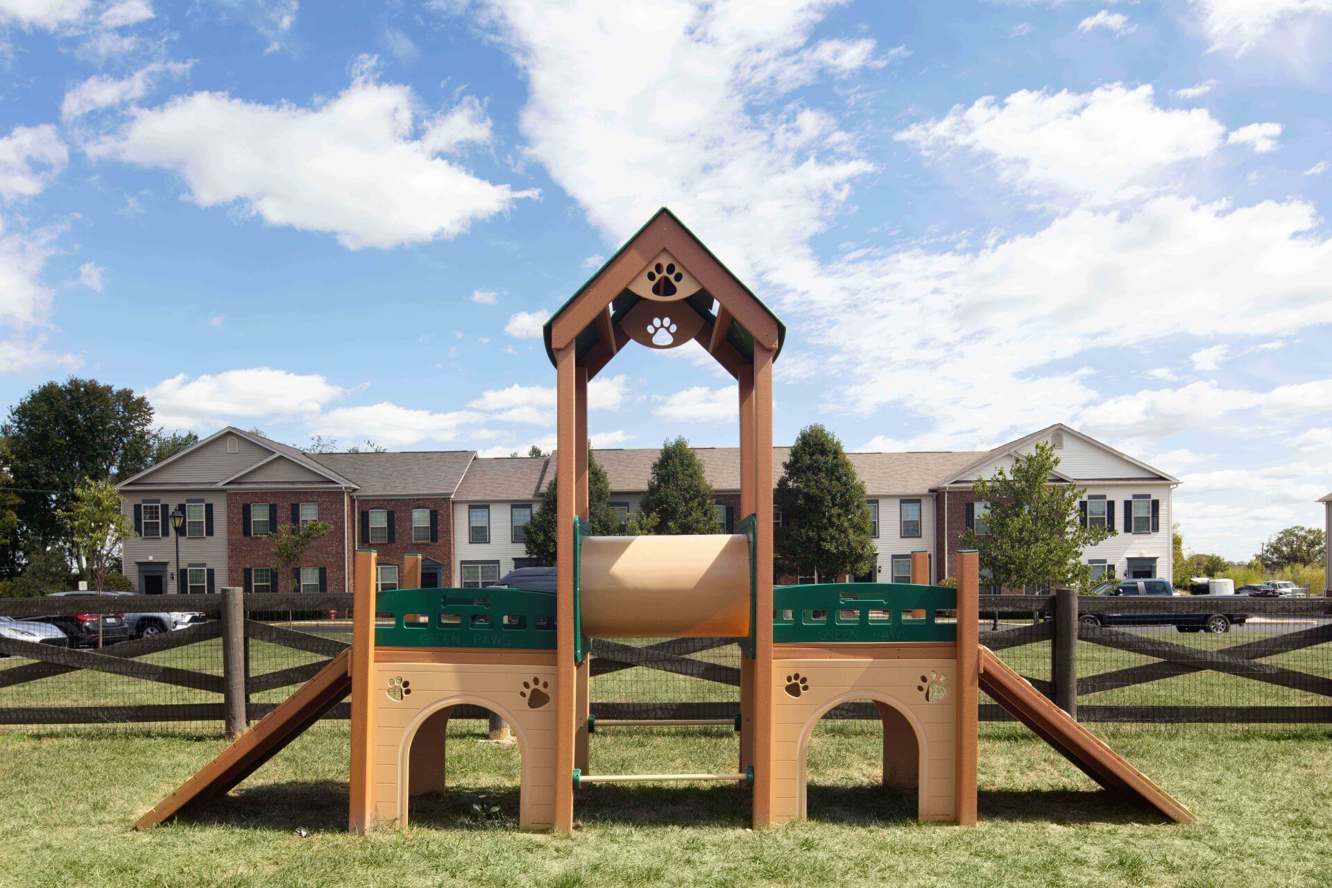 A wooden playground is sitting in the middle of a grassy field in front of a building.