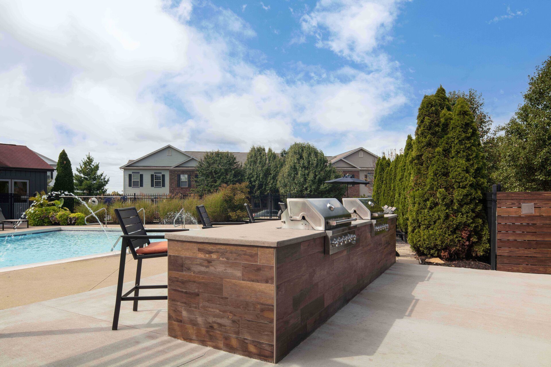 A patio with a grill and a swimming pool in the background.