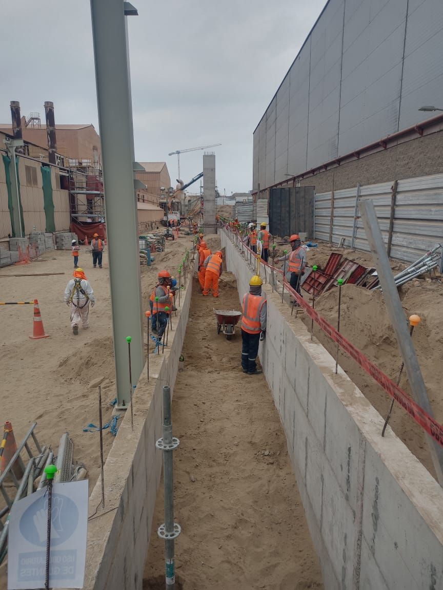 Obreros de la construcción con chalecos naranjas construyen una estructura de hormigón al aire libre, bajo un cielo nublado.