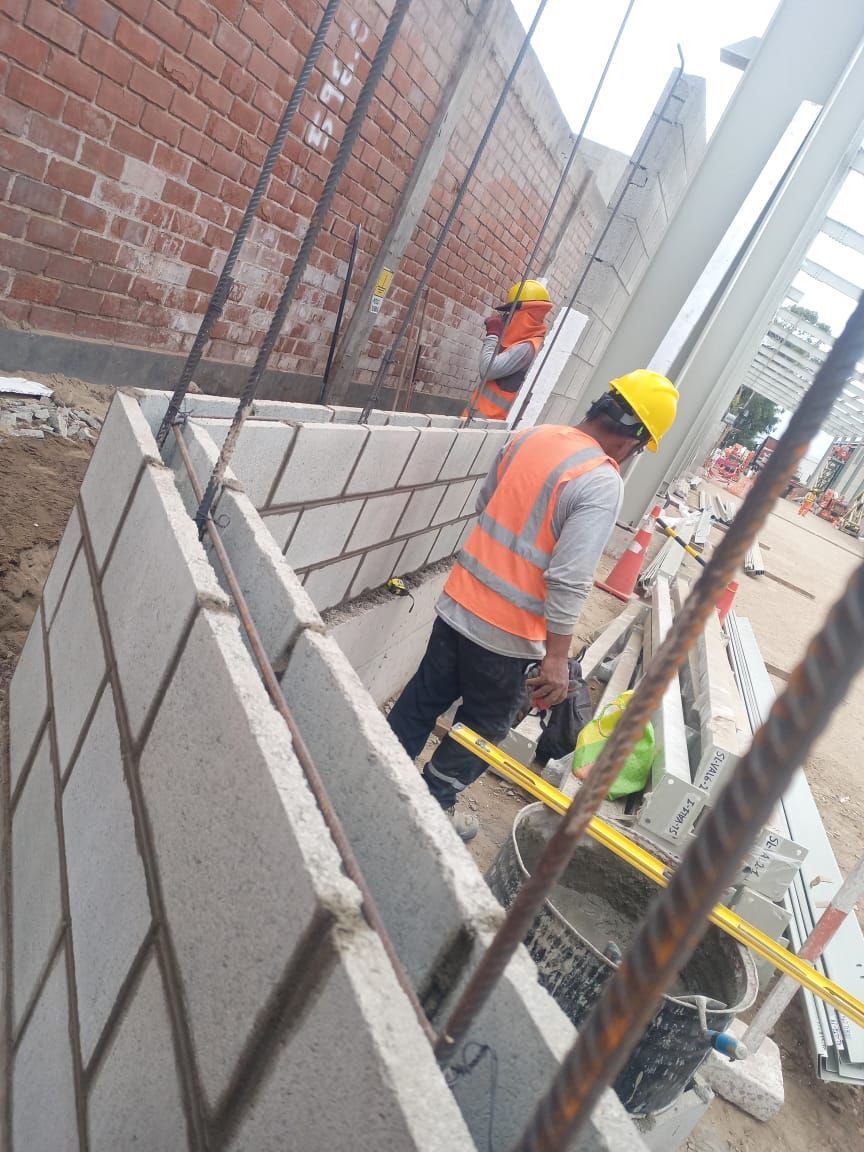 Obreros de la construcción construyen un muro de ladrillos con mortero y herramientas, con chalecos de seguridad y cascos de seguridad. Al aire libre.
