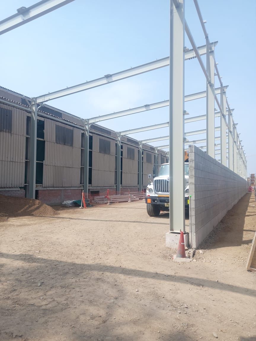 Almacén con estructura de acero en construcción; camión estacionado sobre la grava.