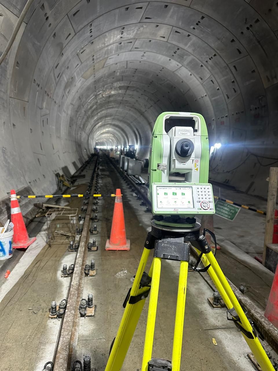 Equipo de topografía instalado en un túnel. Las vías discurren por el suelo. Hay conos y barreras naranjas.