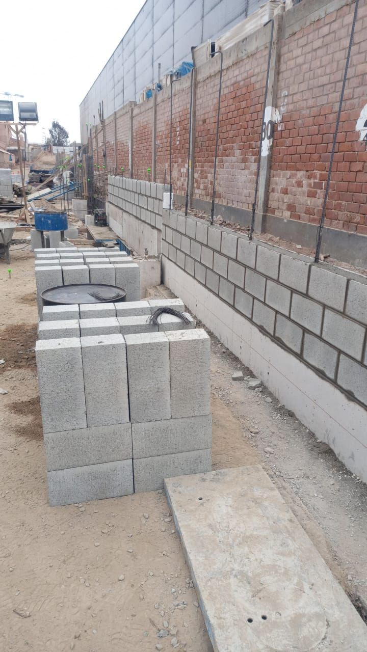 Un trabajador del muelle dirige una grúa amarilla y azul que levanta metal. Cielo azul y costa.
