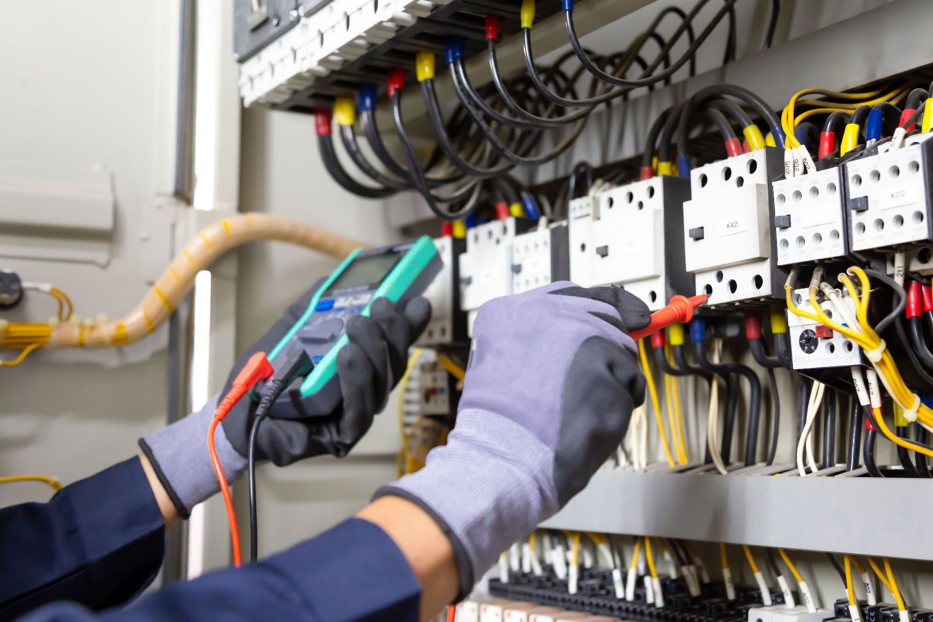 Un electricista con guantes de trabajo prueba el cableado del panel eléctrico con un multímetro.