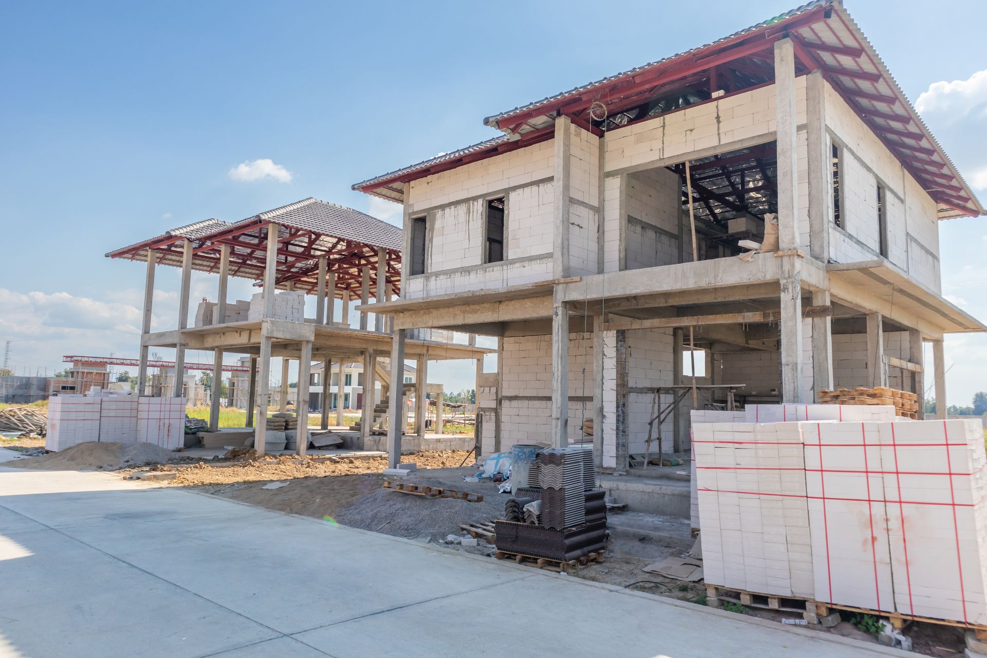 Casas de dos pisos en construcción con estructura expuesta y soportes de hormigón en un día soleado.