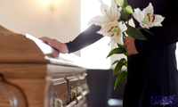 A woman is holding flowers in front of a coffin at a funeral.