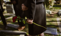 A woman is holding a red rose in her hand in a cemetery.