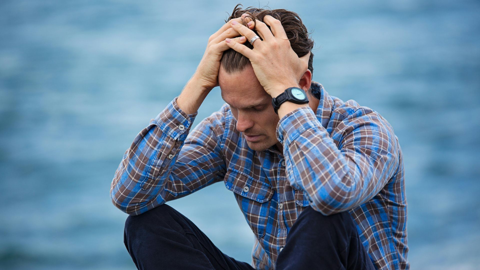 A man is sitting on the beach with his hands on his head.