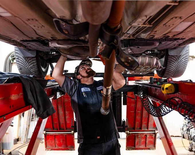 A mechanic working on the underside of a car which is lifted up on a hydraulic jack | Jerry's Auto Repair
