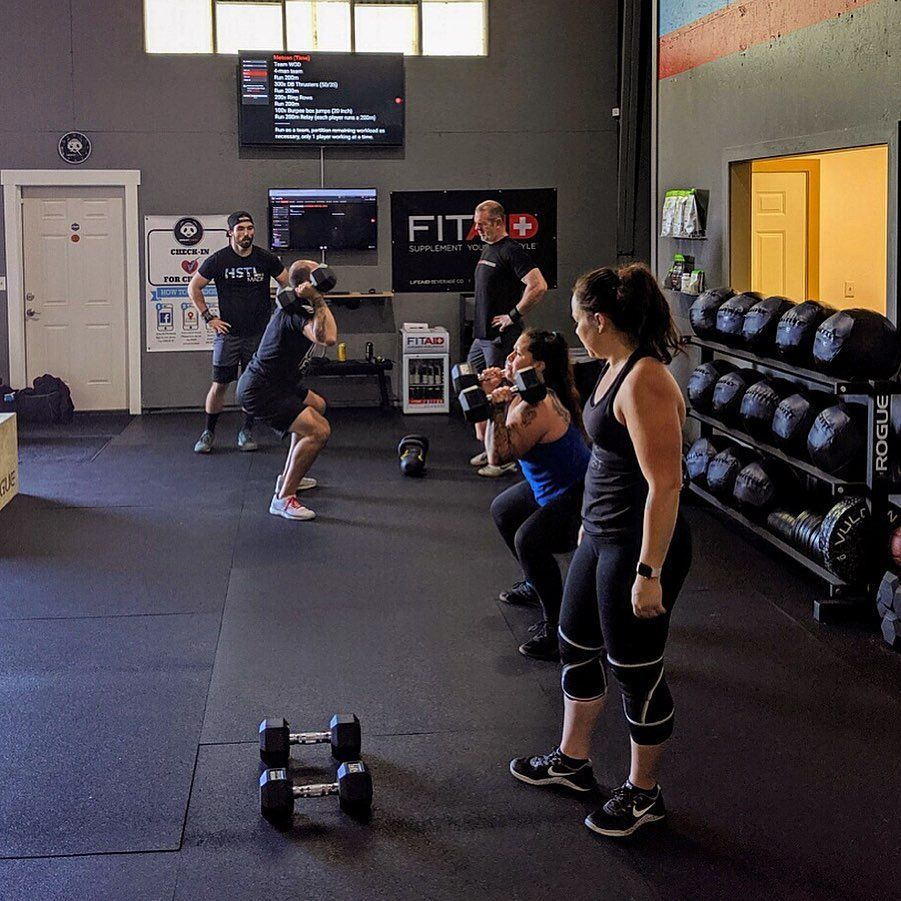 People exercising with weights in a gym. A person does a dumbbell squat as others watch.