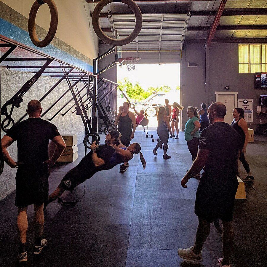 People exercising in a gym with various equipment. One man is doing a gymnastic exercise, being held up by another.