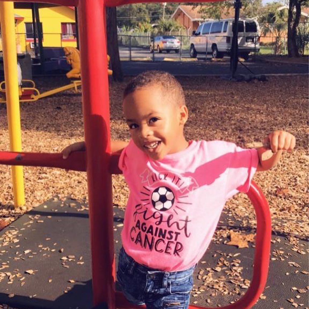 A little boy wearing a pink shirt that says fight against cancer