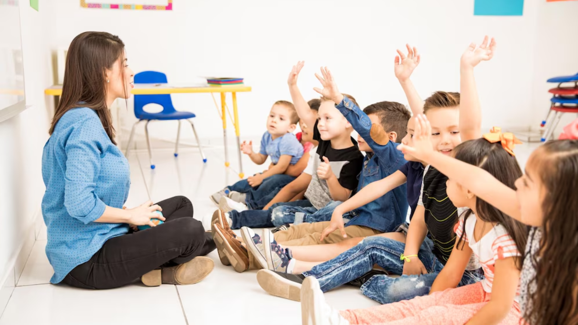 A teacher is sitting on the floor talking to a group of children.