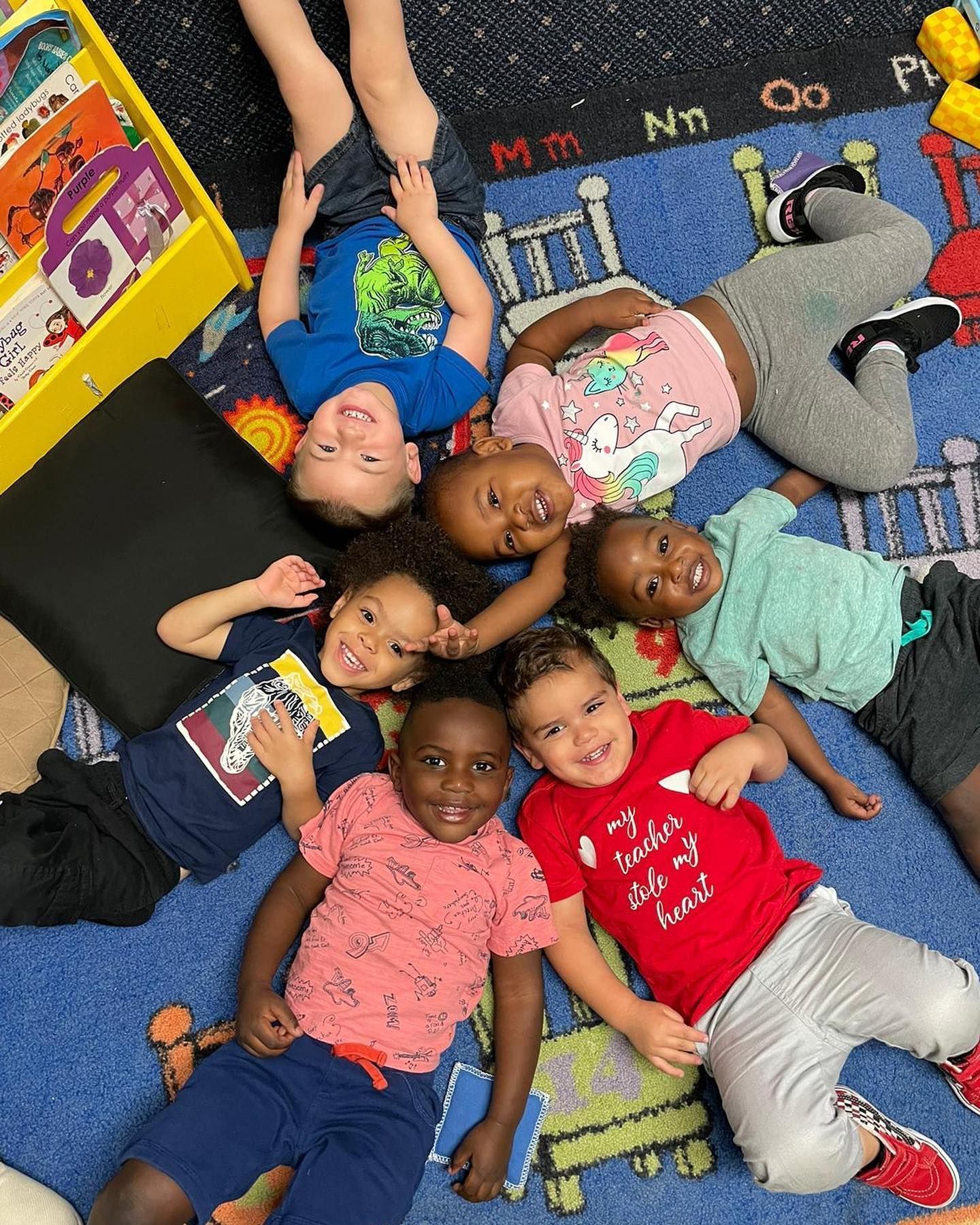 A group of children are laying on the floor in a circle.